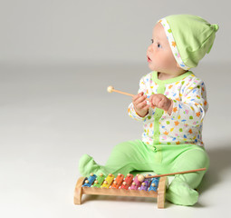 Portrait of Infant child baby boy kid toddler sitting in light green body and play with xylophone...