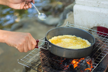 Make an omelette on the pan in hot oil,  place on the stove, prepare breakfast for hiking or camping using as travel concept