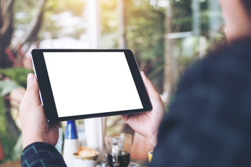 Mockup image of business woman's hands holding black tablet pc with blank desktop white screen in cafe and green nature background