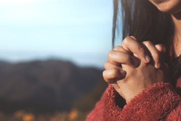 Woman hands folded in prayer in beautiful nature background with sunlight in vintage color tone