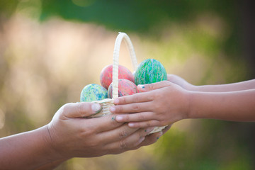 Mother and asian child girl holding basket with colorful Easter eggs together in outdoor