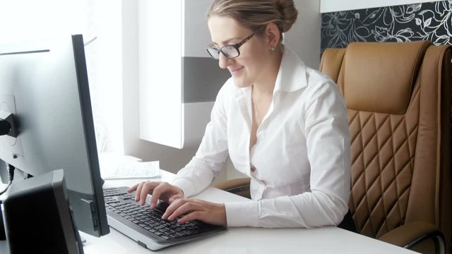 4k footage of beautiful smiling businesswoman sitting behind modern white desk in office and working on computer