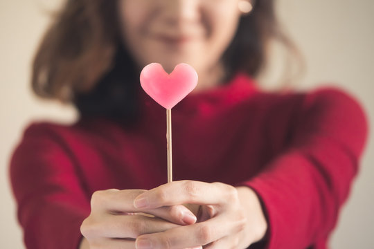 Portrait Of Happy Asian Woman Dressed In Red Sweater Holding Pink Heart Candy.