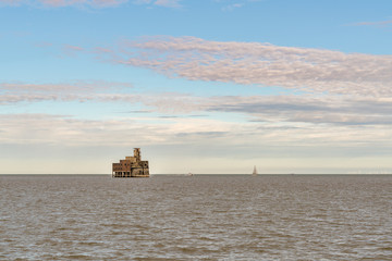 Obraz premium Grain Tower Battery in the River Medway, Isle of Grain, Kent, England, UK - with a sailing boat in the background