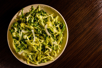 Salad with the savoy cabbage in the dish on dark wooden table. Top view