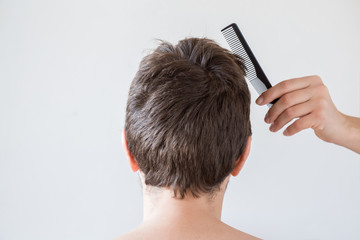 Hairdresser's hand with comb brushing man's dry brown hair on the gray background. Cares about a...