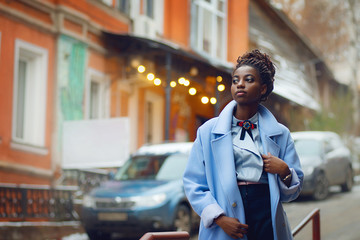 Stylish African girl in the blue coat in the style fashion on the streets with bokeh and cars in the background