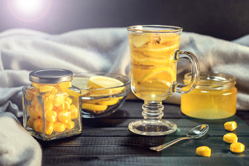 Tea with ginger and lemon in a glass cup and yellow sweets on a wooden background