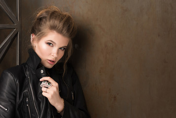 Fototapeta premium Horizontal portrait of young sexy woman in rock. Black leather jacket, an earring and a ring. Collected hair, professional makeup