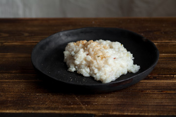 Traditional creamy tender risotto with spicy breadcrumbs in black ceramic plate on wooden table. Copy space.