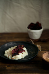 Traditional creamy tender risotto with spicy breadcrumbs and baked savoury beetroot slices in black ceramic plate on wooden table. Vertical composition, side view.
