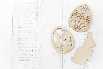 Symbols of Easter wooden decorative eggs and a rabbit on white wooden background. Selective focus. Rustic style. Top view. Place for text.