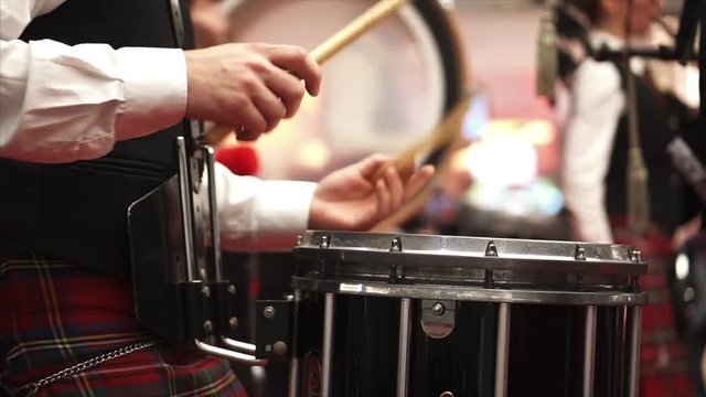 A man in a Scottish kilt plays the drum. Concert. Bagpipes. A man in checkered clothes. Musician at the concert. Drummer