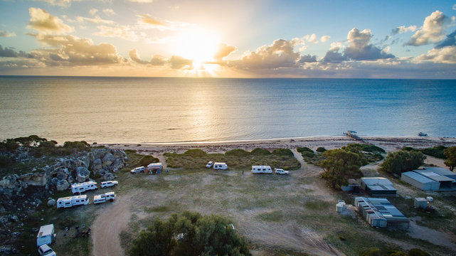Aerial view of four wheel drive vehicles and caravans at a free camp next to a beach and cliffs in the late afternoon