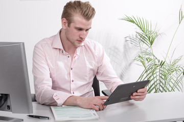 Junger Mann am Schreibtisch hält ein Pad in der Hand und überlegt