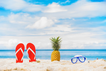 Close up Pineapple, mask and filp flop on the beach with blue sky and sea on background.