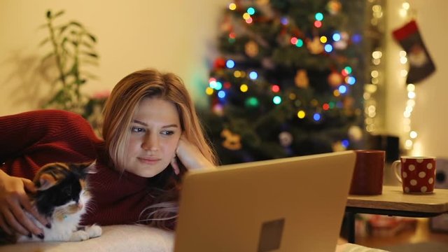 Woman comfortable position bed working new notebook petting orange cat technology addicted people concept nighttime routine young female girl sitting home looking film indoor christmas holiday tree