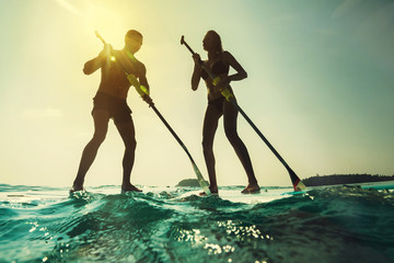 Paddleboarding at sunset. Young couple in the sea with paddle and board.