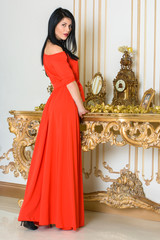 Fototapeta na wymiar Young woman with dark hair in a long red dress in a baroque, Renaissance or Rococo living room. In a luxurious interior
