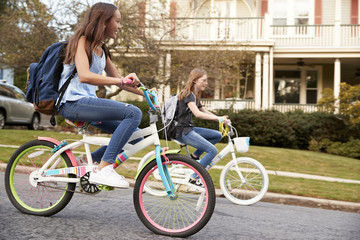 Plakat Two teen girls riding bikes in street, side view close up