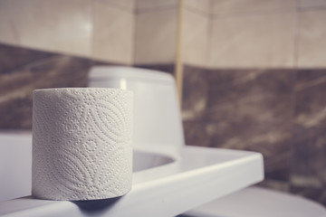 a roll of toilet paper on the background of toilet. On the edge of the bath. The tiles and the toilet in the background blur.