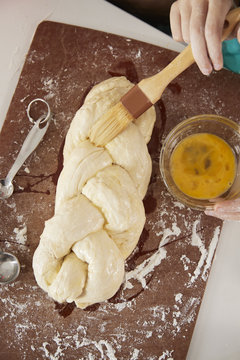 Girl Glazing Plaited Challah Dough With Mum, Overhead Close Up