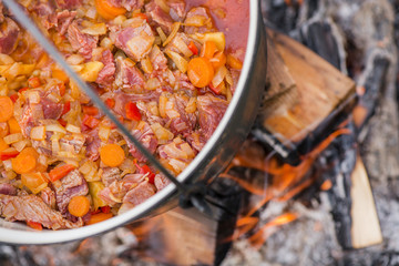 Boiling, hot goulash soup with meat, paprika, potatoes, onion, carrots is the traditional dish of Hungarian cuisine. Meat stew being prepared in crock pot on open fire. Picnic at the weekend in nature
