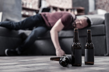 Alcoholic drink. Selective focus of beer bottles standing on the floor with bearded man sleeping in...