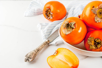 Delicious raw ripe persimmon fruit on white marble background copy space