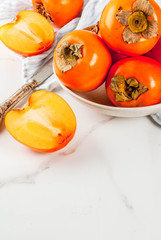 Delicious raw ripe persimmon fruit on white marble background copy space