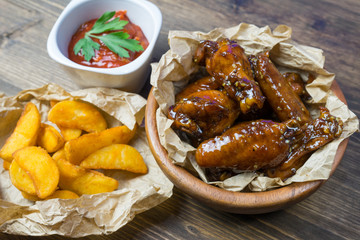 Chicken wings in a fragrant and pungent sauce with sesame seeds. A glass of fresh cold beer and fried potatoes with rustic tomato sauce from fresh tomatoes and herbs