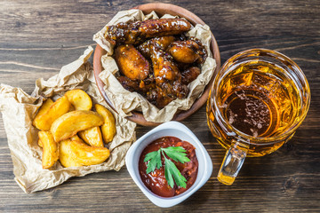 Chicken wings in a fragrant and pungent sauce with sesame seeds. A glass of fresh cold beer and fried potatoes with rustic tomato sauce from fresh tomatoes and herbs