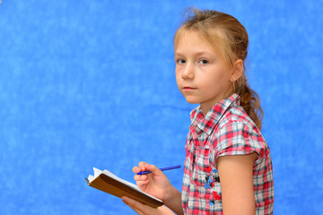 Pupil in pink dress with braids and pencils in hair. Back to school and education concept. Girl and female hands hold blue notebook. School girl with happy smiling face isolated on blue background