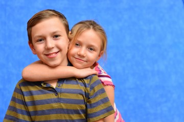 Cute couple of kids in casual clothes are giving high five, looking at camera and smiling, on gray background