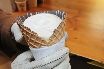 Closeup of woman girl hands in white gloves holding a cornettoccino, coffee with ice cream and milk in a waffle cone with chocolate. Hot drink in a street, lifestile urban love relationship and dating