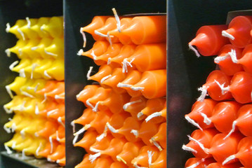 Many multicolored colorful red orange yellow paraffin stick candles arranged in black shelves lying on shelter and sorted by color in a household candle shop store market. Selected focus.