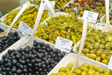 Variety assortment diverse of fresh healthy tasty green and black olives in white plastic bowls for sale on open street city market in Stuttgart, Germany.