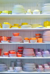 Bright colorful yellow red dishes, plates and cups standing on white shelf. Concept of buying choosing new dishes for house home, interior indoor decoration o for gifts. Clean ordered dishes in store.