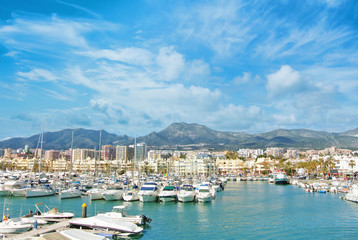 Fototapeta na wymiar Benalmadena Puerto Marina sport port, a view to piers with white modern luxury sport yachts, Mediterranean sea and mountains and cloudy sky at the background. Spain winter relax vacation concept.