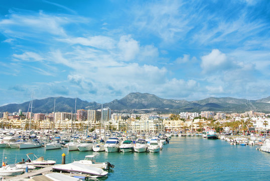 Benalmadena Puerto Marina sport port, a view to piers with white modern  luxury sport yachts, Mediterranean sea and mountains and cloudy sky at the  background. Spain winter relax vacation concept. Stock Photo