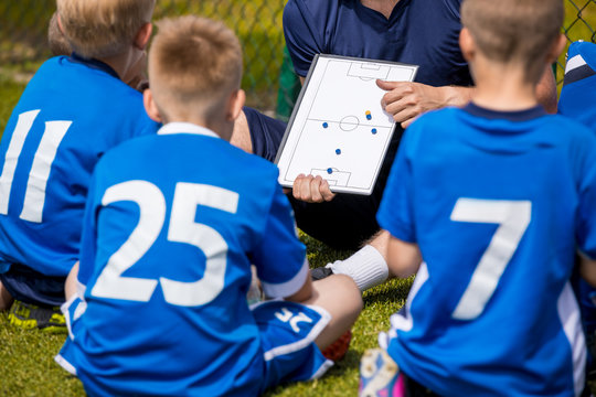 Coaching Kids Soccer. Football Team with Coach at the Stadium. Boys Listening to Coach's Instructions Before Competition. Coach Giving Team Talk Using Soccer Tactics Board