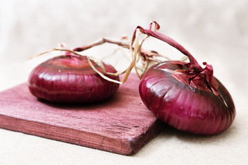 Crimean sweet onion on a old wooden board on light blurred background. Two whole large round bulbs. Red onion fragrant ingredient for salads. Selective focus.