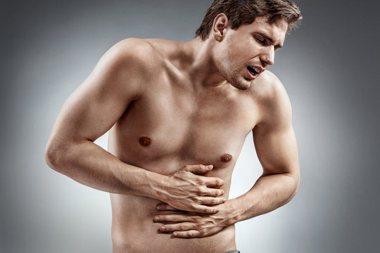 Abdominal pain. Young man holding his stomach in pain. Medical concept.