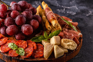 Prosciutto, sausage, wine, grape, parmesan on dark table.