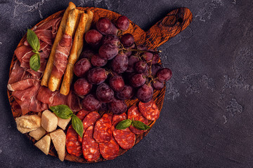 Prosciutto, sausage, wine, grape, parmesan on dark table.