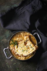 Traditional french onion soup with cheese and bread served in vintage aluminum pan with rosemary and textile napkin over dark metal background. Top view, copy space