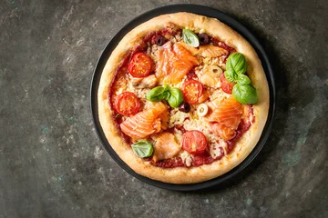 Fotobehang Pizzeria Traditionele pizza met gerookte zalm, kaas, tomaten en basilicum geserveerd op zwarte plaat over oude donkere metalen achtergrond. Bovenaanzicht met ruimte. Rustieke stijl