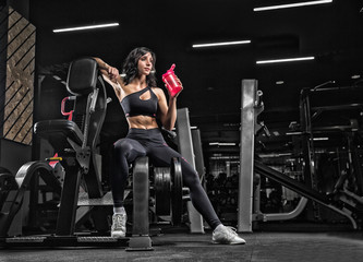 Beautiful young girl athlete bodybuilder, sitting in the gym, resting after the crossfit, drinking sports nutrition, protein. Personal trainer. - 186860868