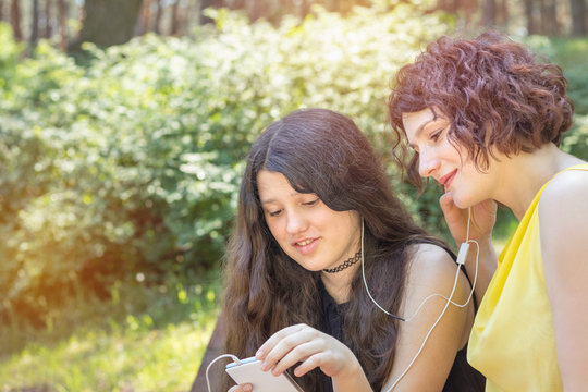 Mother and teenage daughter listening to music together in the city park on a summer sunny day. Walking in summer park on the summer day. Copy space