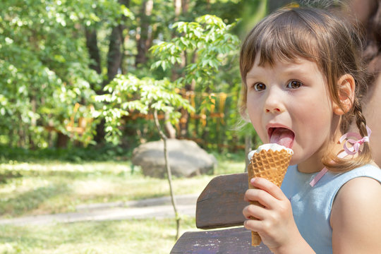 Cute little girl eating ice-cream in the city park on a summer sunny day. Portrait little girl with copy space.